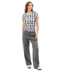 Woman wearing an All Eyes On Me Print Tee featuring colorful eye and celestial symbols all over a white cotton fabric paired with gray wide-leg pants and sneakers.