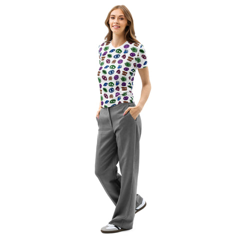 A woman wearing the All Eyes On Me Print Tee with colorful eye and mouth patterns on a white cotton crew neck fabric, paired with gray trousers and casual shoes.