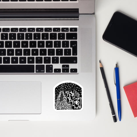 As Above, So Below Sticker (B&W) featuring intricate black and white celestial and occult-inspired design on durable high-opacity vinyl, placed on a laptop corner next to pencil, pen, and phone.