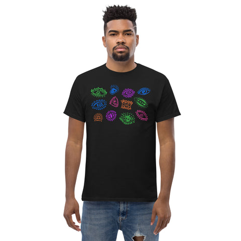 Man wearing a black "All Eyes On Me Tee" made of premium heavyweight fabric, featuring colorful graphic eyes in blue, green, purple, and orange across the chest, styled with casual ripped jeans.