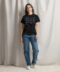 A person stands wearing the All Eyes On Me Tee in solid black, featuring colorful eye and mystical symbol designs on the chest, paired with casual blue jeans and white sneakers.
