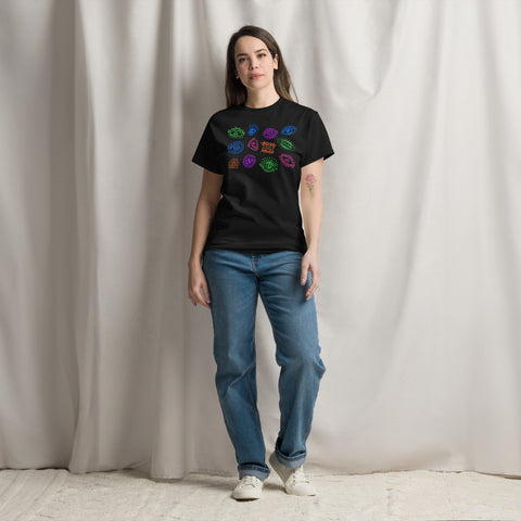 A person stands wearing the All Eyes On Me Tee in solid black, featuring colorful eye and mystical symbol designs on the chest, paired with casual blue jeans and white sneakers.