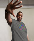 Man wearing a charcoal heavyweight fabric "All Eyes On Me Tee" with colorful eye symbols printed across the chest, reaching forward with hand extended in confident pose.