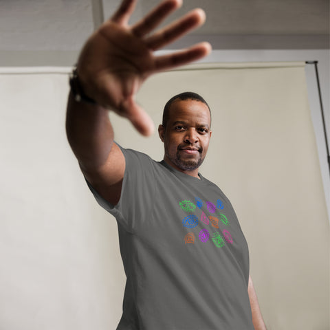 Man wearing a charcoal heavyweight fabric "All Eyes On Me Tee" with colorful eye symbols printed across the chest, reaching forward with hand extended in confident pose.
