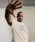 Man wearing a premium heavyweight solid color All Eyes On Me Tee with colorful eye symbols printed on the front, reaching hand toward the camera against a neutral background