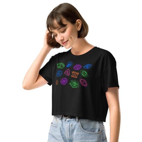 A woman wearing the black All Eyes on Me Crop Top featuring colorful eye and symbol designs, paired with light blue high-waisted jeans, styled with a relaxed, dark feminine aesthetic.